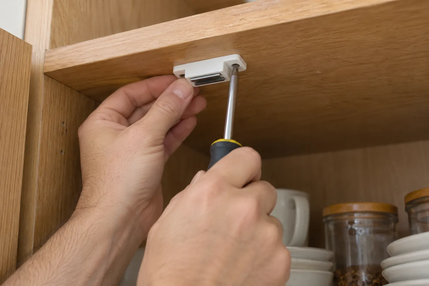 Cabinet catch being adjusted inside a kitchen cupboard